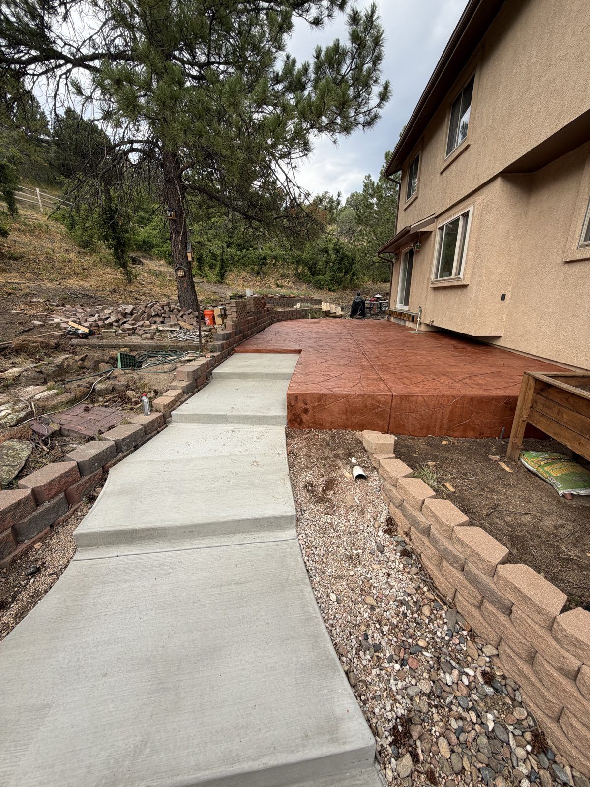 Broom-finish concrete walkway beside a timber retaining wall and pine trees